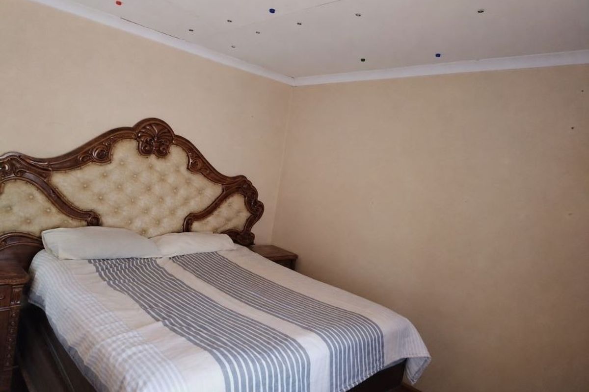 A bedroom featuring plain walls and a ceiling with visible surface imperfections.