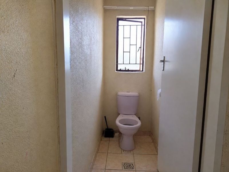 A compact, functional bathroom featuring a standard toilet, tiled flooring, and a window with a security gate.