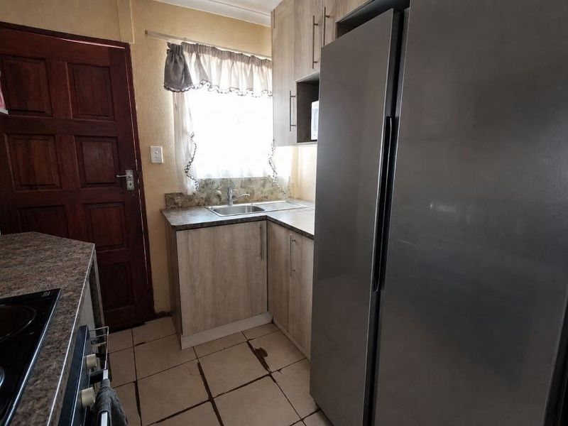 Compact kitchen featuring laminate cabinetry, stone-look countertops, stainless steel sink, and ceramic tiled flooring with visible wear.