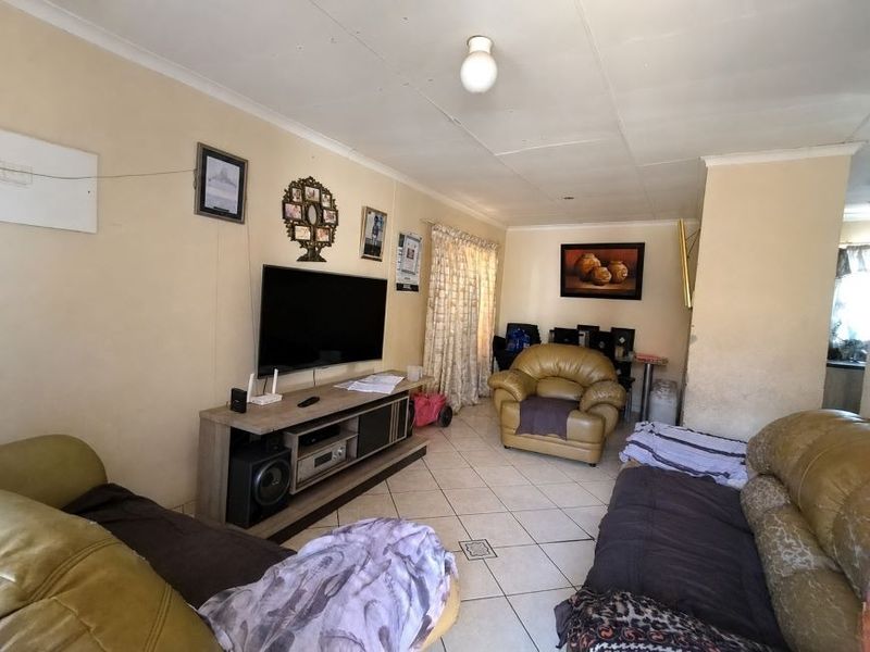 A living room featuring tiled flooring and coved ceilings, offering a functional space that would benefit from cosmetic updates to the walls and finishes.