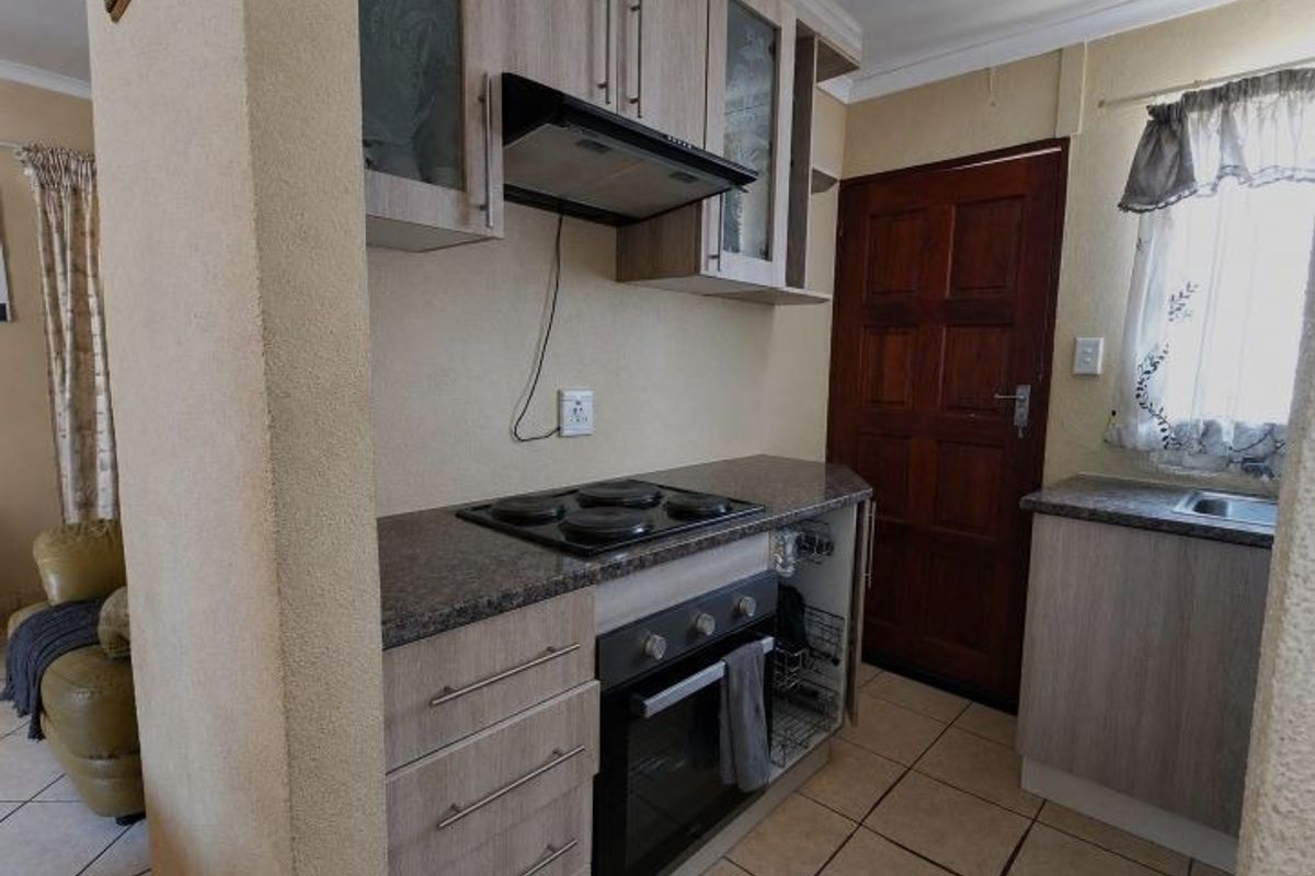 Compact kitchen featuring light wood-finish cabinetry, granite-look laminate countertops, built-in oven and hob, and tiled flooring with direct access to an exterior door.