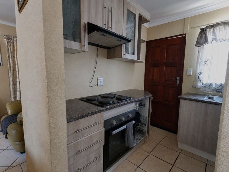 Compact kitchen featuring light wood-finish cabinetry, granite-look laminate countertops, built-in oven and hob, and tiled flooring with direct access to an exterior door.