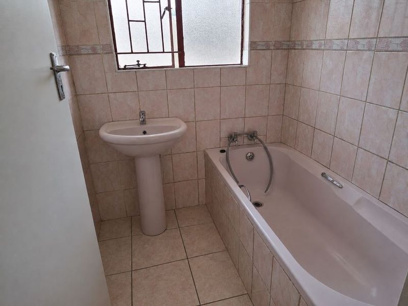 A functional bathroom featuring a pedestal basin, a built-in bathtub, and full-height wall tiling.