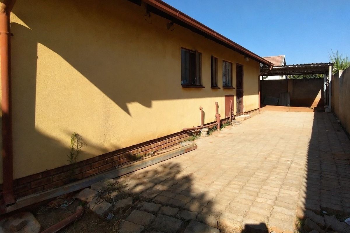 Rear exterior view of the property featuring a paved driveway, brick plinth detailing, and an attached carport structure.