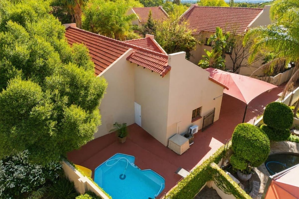 Aerial view of the property featuring a swimming pool, paved patio area with shade sail, and well-maintained garden surroundings.