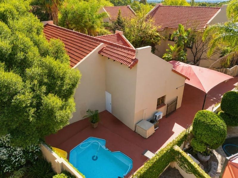 Aerial view of the property featuring a swimming pool, paved patio area with shade sail, and well-maintained garden surroundings.