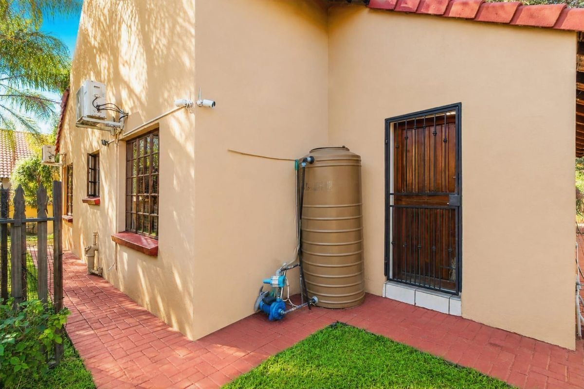 Rear exterior view featuring a water storage tank with pump, security gate, and paved walkway along the side of the house.