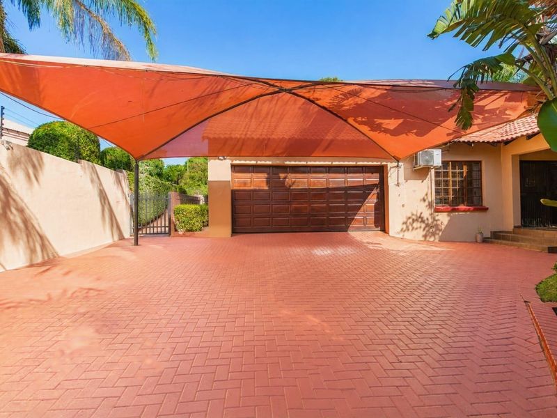 Front exterior view featuring a paved driveway, a large orange shade sail, and a wooden garage door with an external air conditioning unit.
