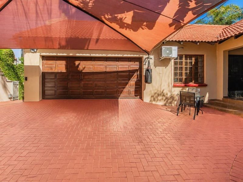 Front exterior view featuring a paved driveway, a large shade sail covering the garage area, and a tiled roof structure.