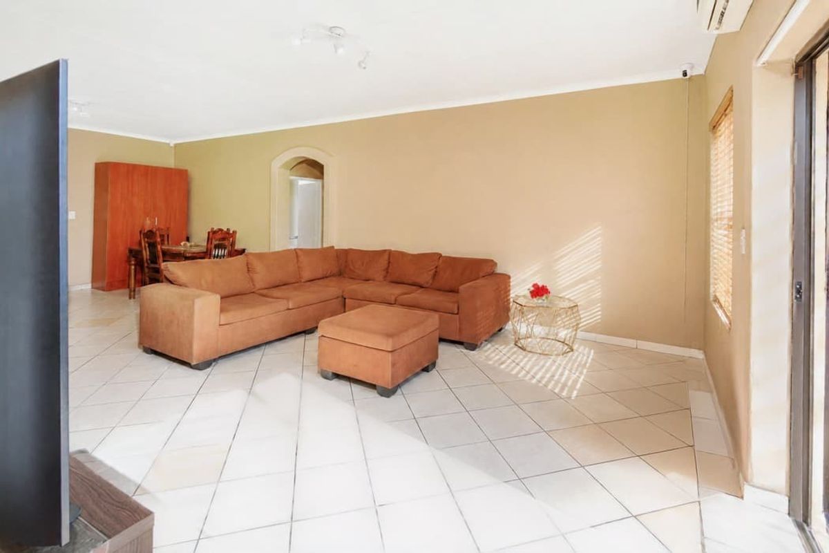 Spacious living area featuring neutral tiled flooring, an arched entryway, and a wall-mounted air conditioning unit with access to an outdoor area.