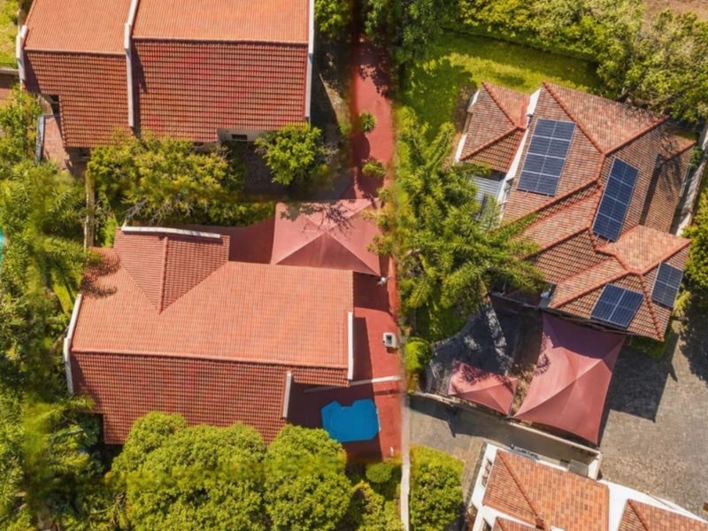 Aerial view of the property showcasing the tiled roof structure, integrated solar panels, swimming pool, and surrounding landscaped garden areas.