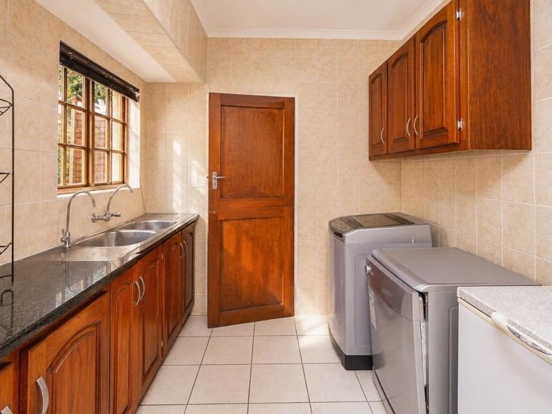 A functional laundry room featuring tiled walls and flooring, wooden cabinetry, granite countertops, and a double basin sink.