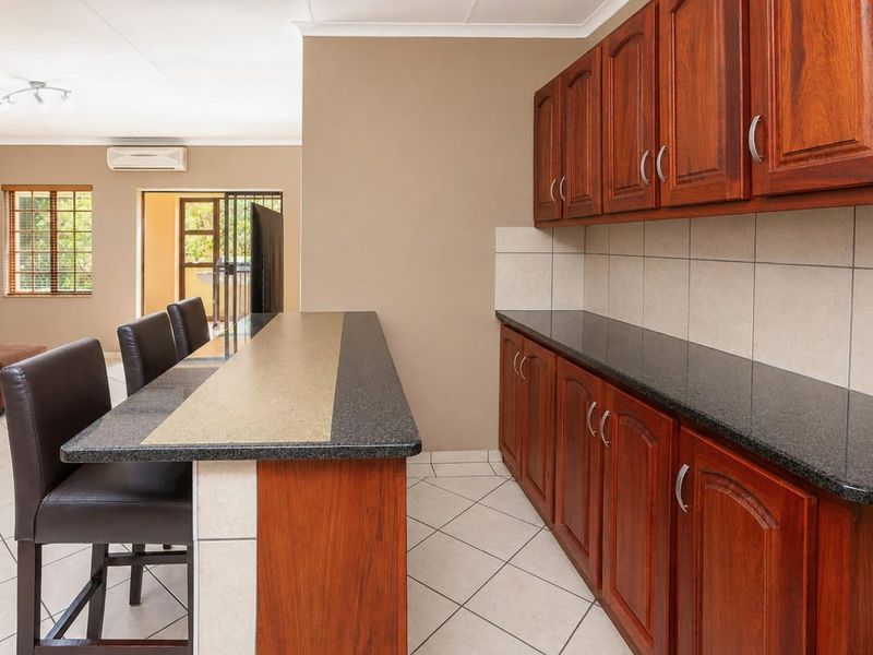 Open-plan kitchen area featuring dark wood cabinetry, granite countertops, a breakfast bar, and tiled flooring, seamlessly connecting to the adjacent living space.