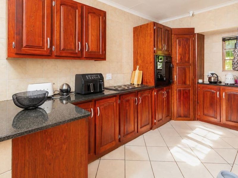 A functional kitchen featuring warm-toned wooden cabinetry, dark granite countertops, built-in oven, electric hob, and neutral tiled flooring.