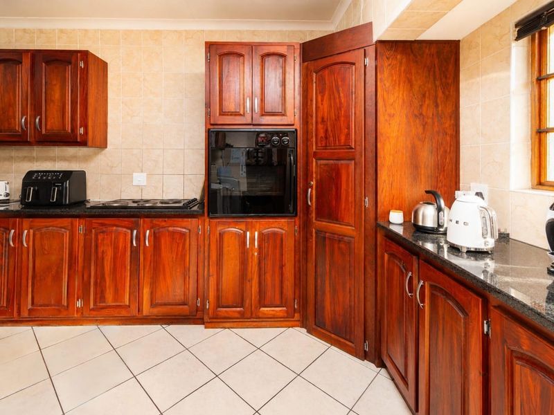 A functional kitchen featuring warm-toned wooden cabinetry, dark granite countertops, a built-in oven, and a ceramic hob with tiled backsplash and flooring.