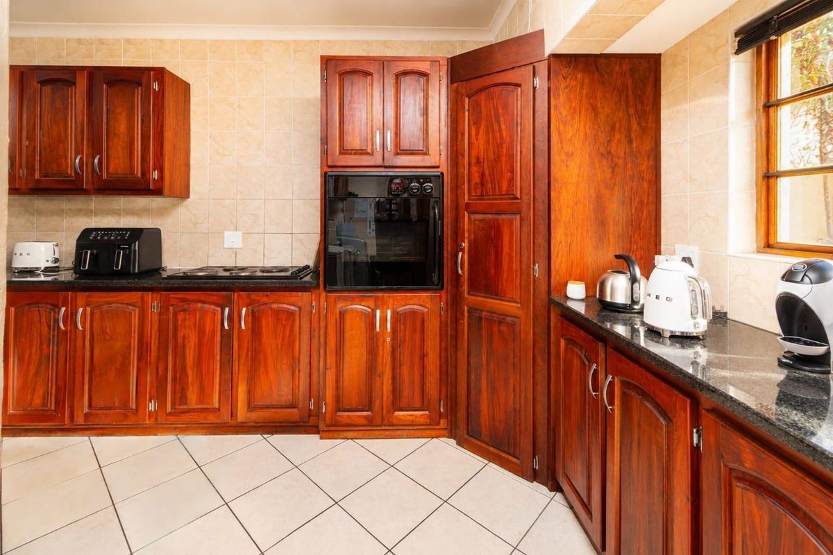 A functional kitchen featuring warm-toned wooden cabinetry, dark granite countertops, a built-in oven, and a ceramic hob with tiled backsplash and flooring.