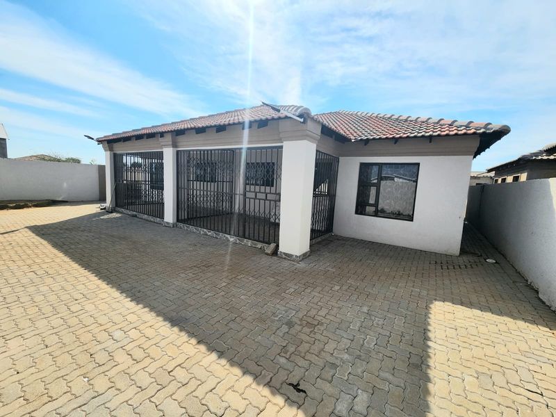 Front exterior view of a single-story house featuring a tiled roof, paved driveway, and secure metal gates over the entrance area.