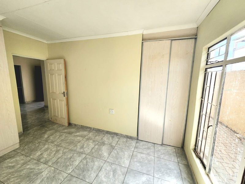 An empty bedroom featuring tiled flooring, a built-in wardrobe, and security bars on the window.