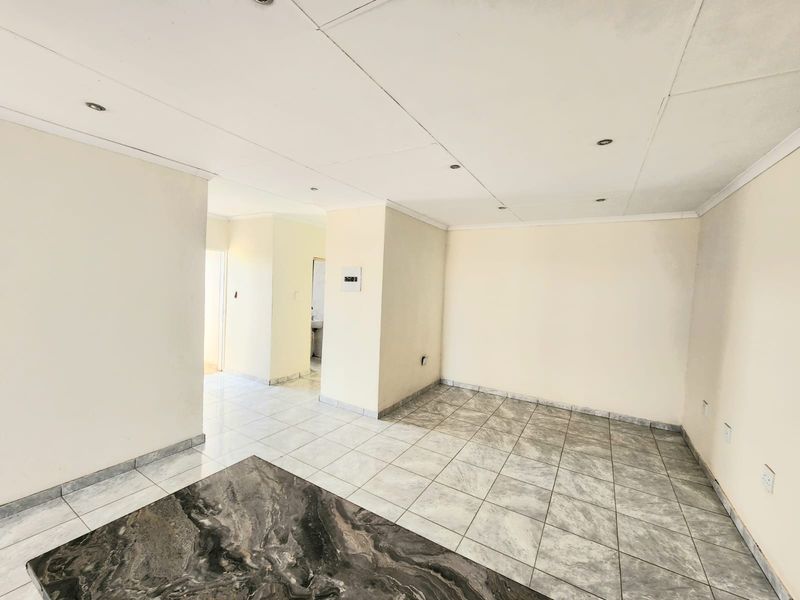 An empty open-plan living area featuring neutral tiled flooring, recessed downlighting, and a clean, blank canvas layout ready for personalization.