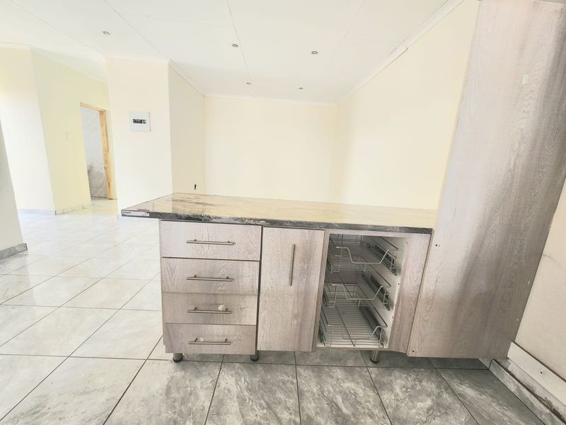 An empty kitchen area featuring a modern island with stone countertops, light wood-finish cabinetry, and tiled flooring throughout.