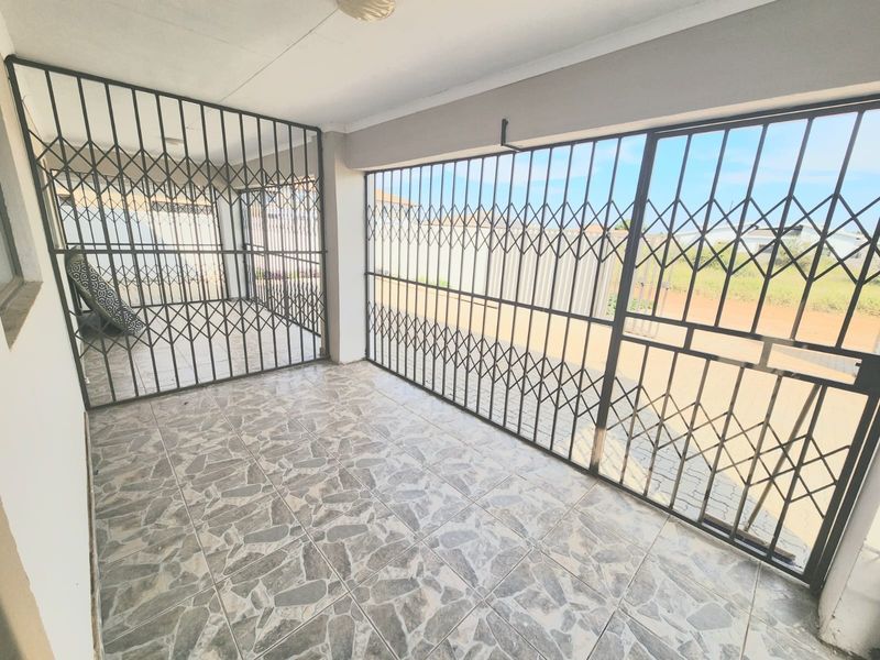 A covered patio area featuring tiled flooring and full-length security gates, providing a secure and functional outdoor space.