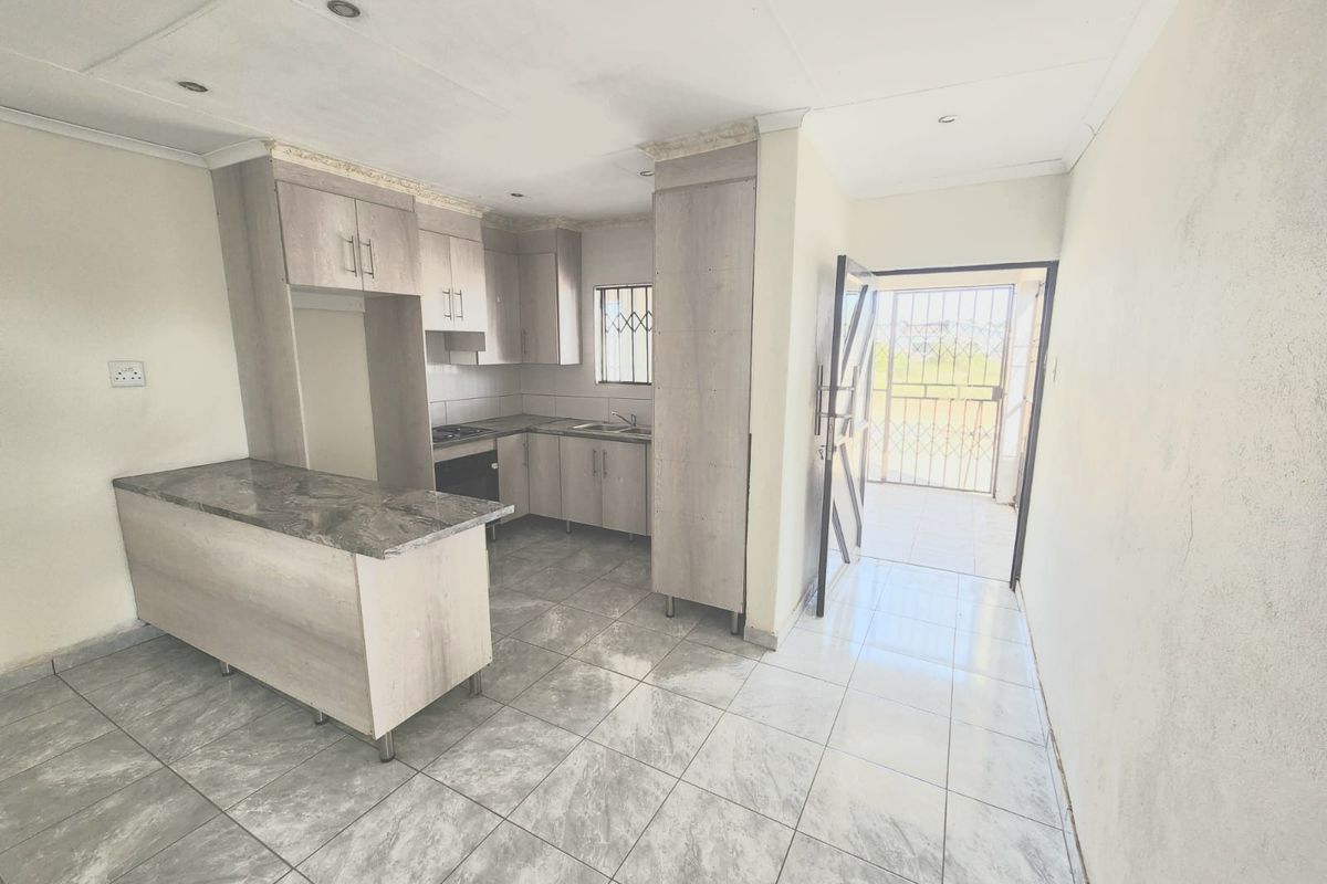 A compact, empty kitchen featuring modern grey cabinetry, a breakfast bar, stone-look countertops, and tiled flooring with direct access to an exterior security gate.