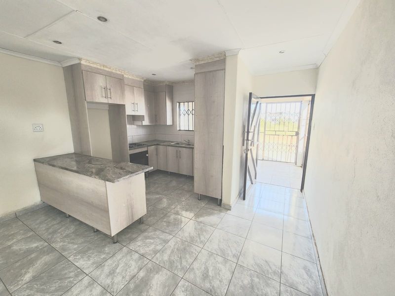 A compact, empty kitchen featuring modern grey cabinetry, a breakfast bar, stone-look countertops, and tiled flooring with direct access to an exterior security gate.