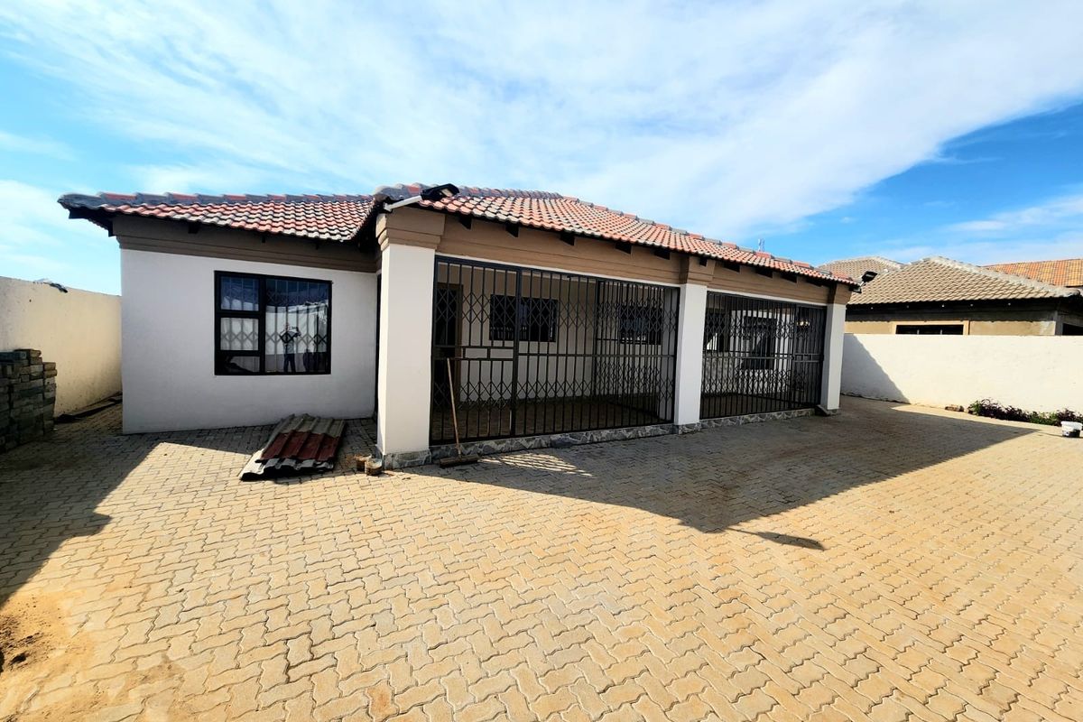 Rear exterior view of the house featuring a tiled roof, paved courtyard area, and security gates installed on the patio.
