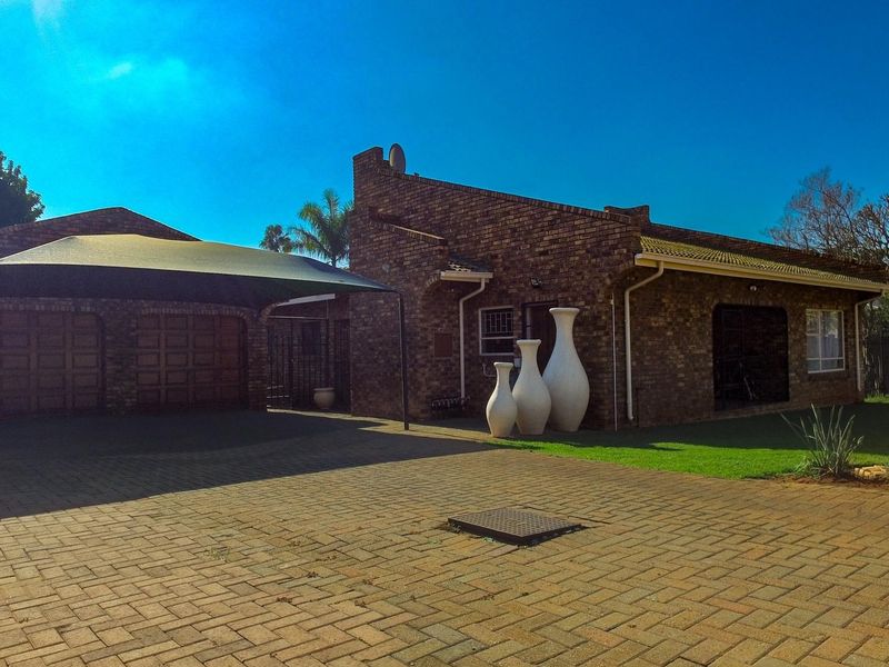 Front view of a face brick house featuring a paved driveway, double garage, and a shade cloth carport.