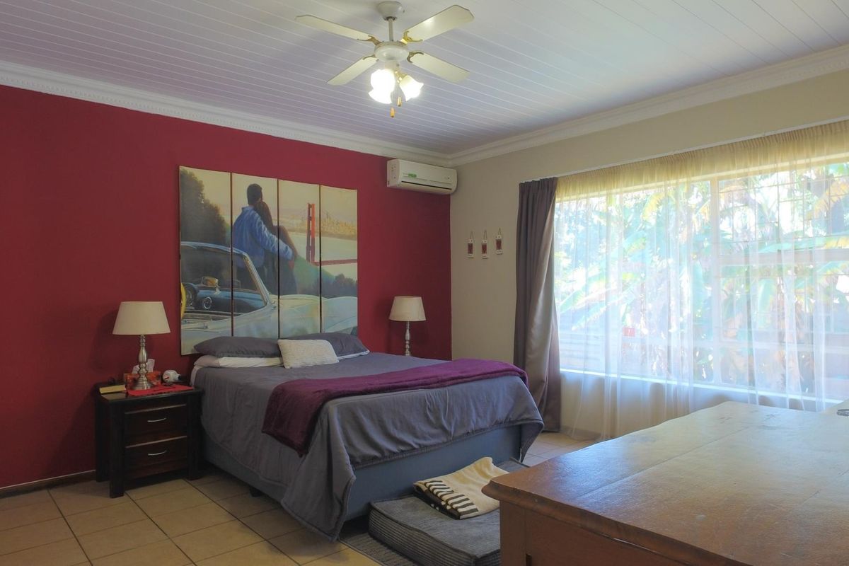 Spacious bedroom featuring tiled flooring, a ceiling fan, and a wall-mounted air conditioning unit, with large windows providing natural light.