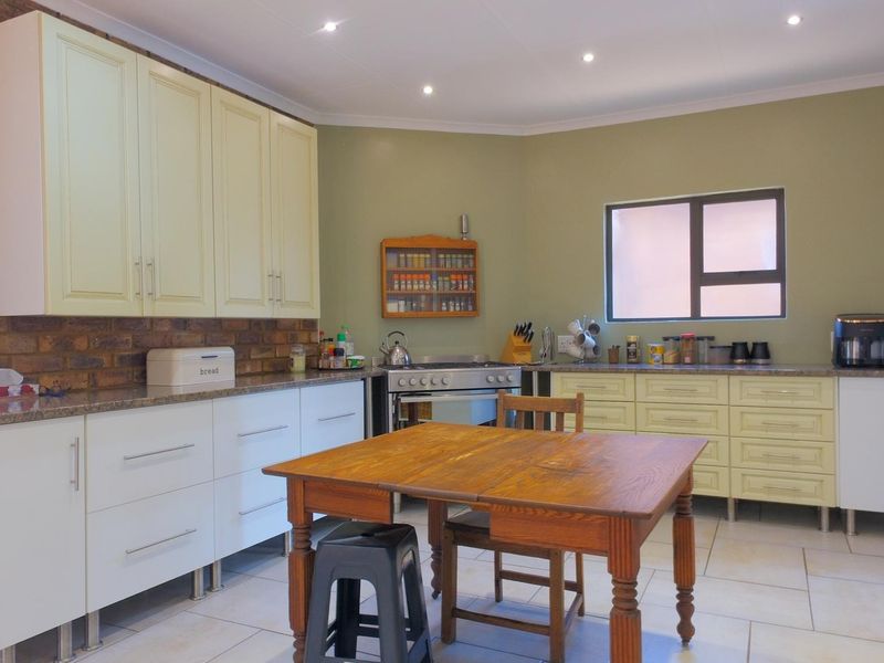 Spacious kitchen featuring a mix of white and cream cabinetry, granite countertops, an exposed brick feature wall, and modern tiled flooring.