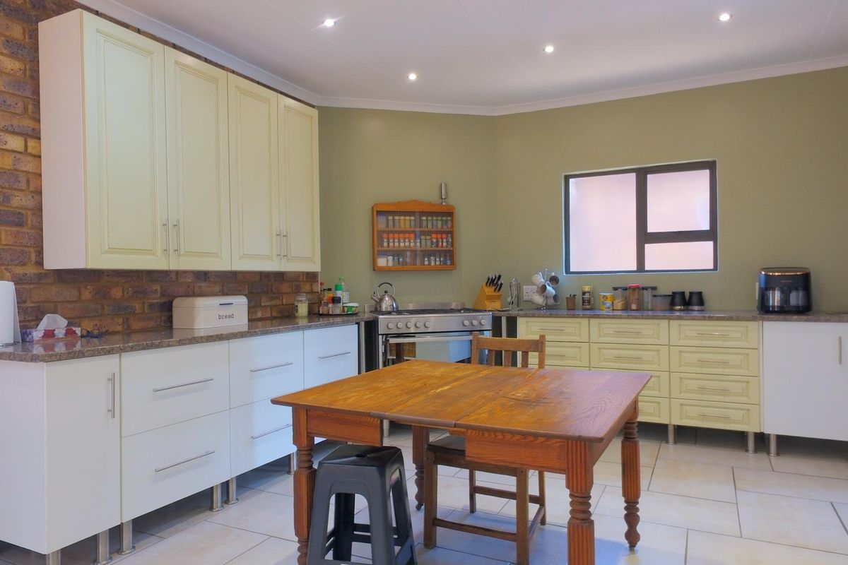 Spacious kitchen featuring a mix of white and cream cabinetry, granite countertops, an exposed brick feature wall, and modern tiled flooring.