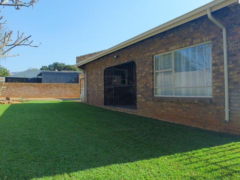 A view of the rear exterior featuring a well-maintained lawn, face brick facade, and secure access point.