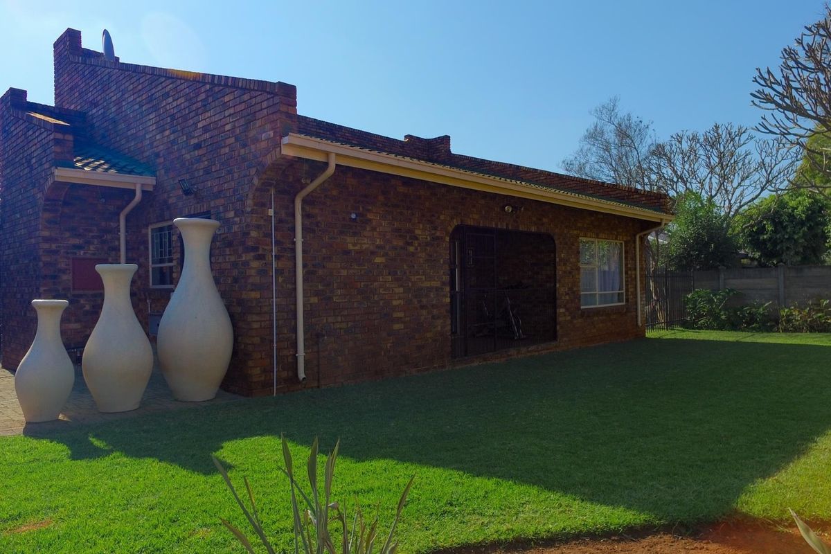 Rear view of a face brick house featuring a paved patio area, well-maintained lawn, and secure access points.