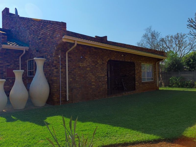 Rear view of a face brick house featuring a paved patio area, well-maintained lawn, and secure access points.