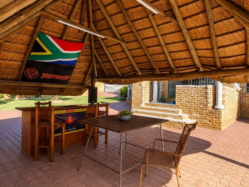 A spacious outdoor entertainment area featuring a traditional thatched roof, exposed timber structure, and a built-in bar, set on a paved patio.