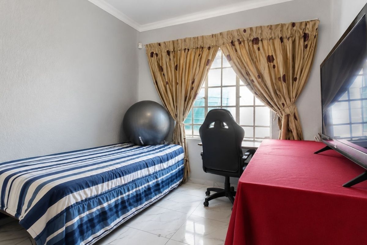 A functional bedroom featuring tiled flooring, a window with security bars, and neutral wall finishes.