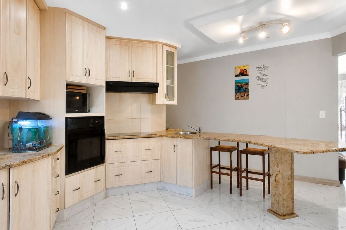 A functional kitchen featuring light wood cabinetry, granite countertops, a breakfast bar, integrated oven, and modern tiled flooring.