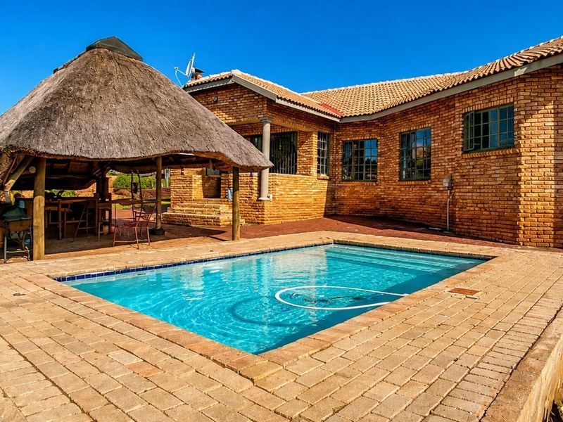 Outdoor entertainment area featuring a swimming pool with brick paving and a traditional thatched lapa, set against a face brick house exterior.
