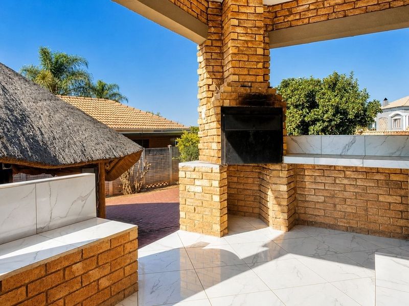 Covered outdoor patio featuring a built-in brick braai, tiled surfaces, and durable flooring, ideal for alfresco dining and entertaining.