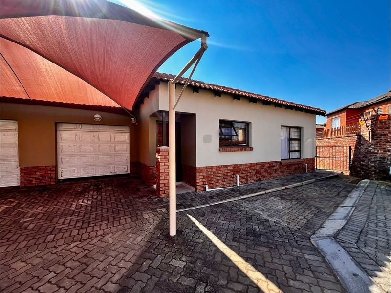 Front elevation of a townhouse featuring a paved driveway, shade sail carport, and a single garage with brick and plaster exterior finishes.