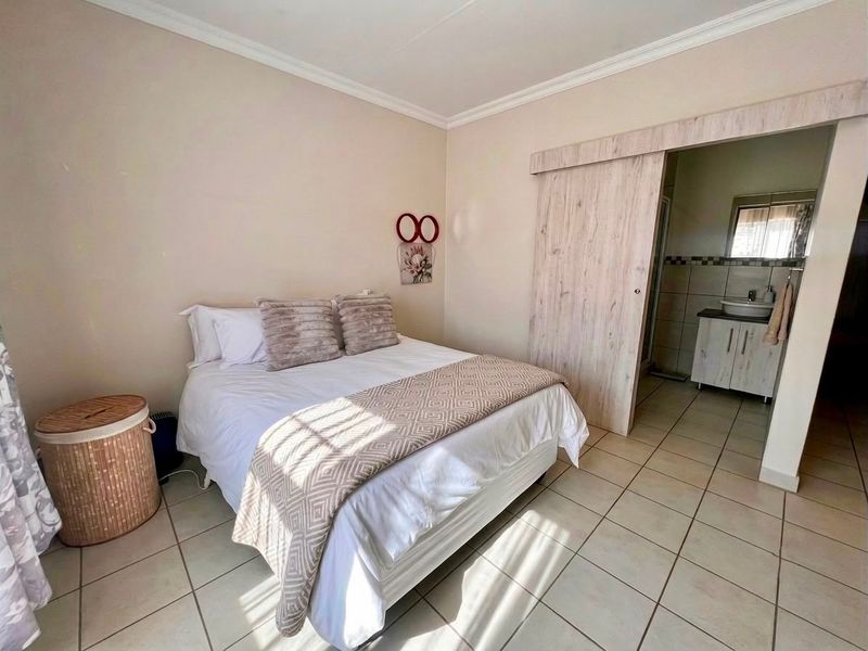 A well-maintained bedroom featuring tiled flooring, crown molding, and a sliding barn door providing direct access to an en-suite bathroom.