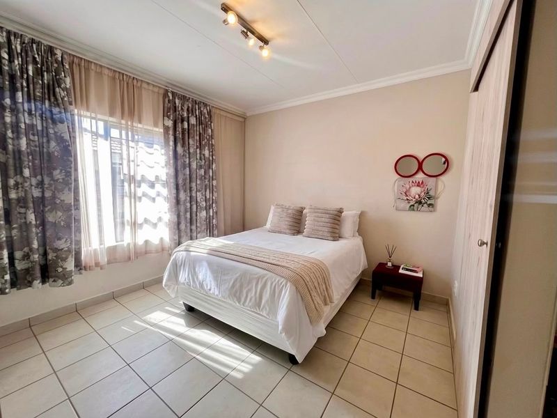 A well-maintained bedroom featuring neutral tiled flooring, built-in cupboards, and a ceiling-mounted spotlight fixture, offering a clean and functional living space.