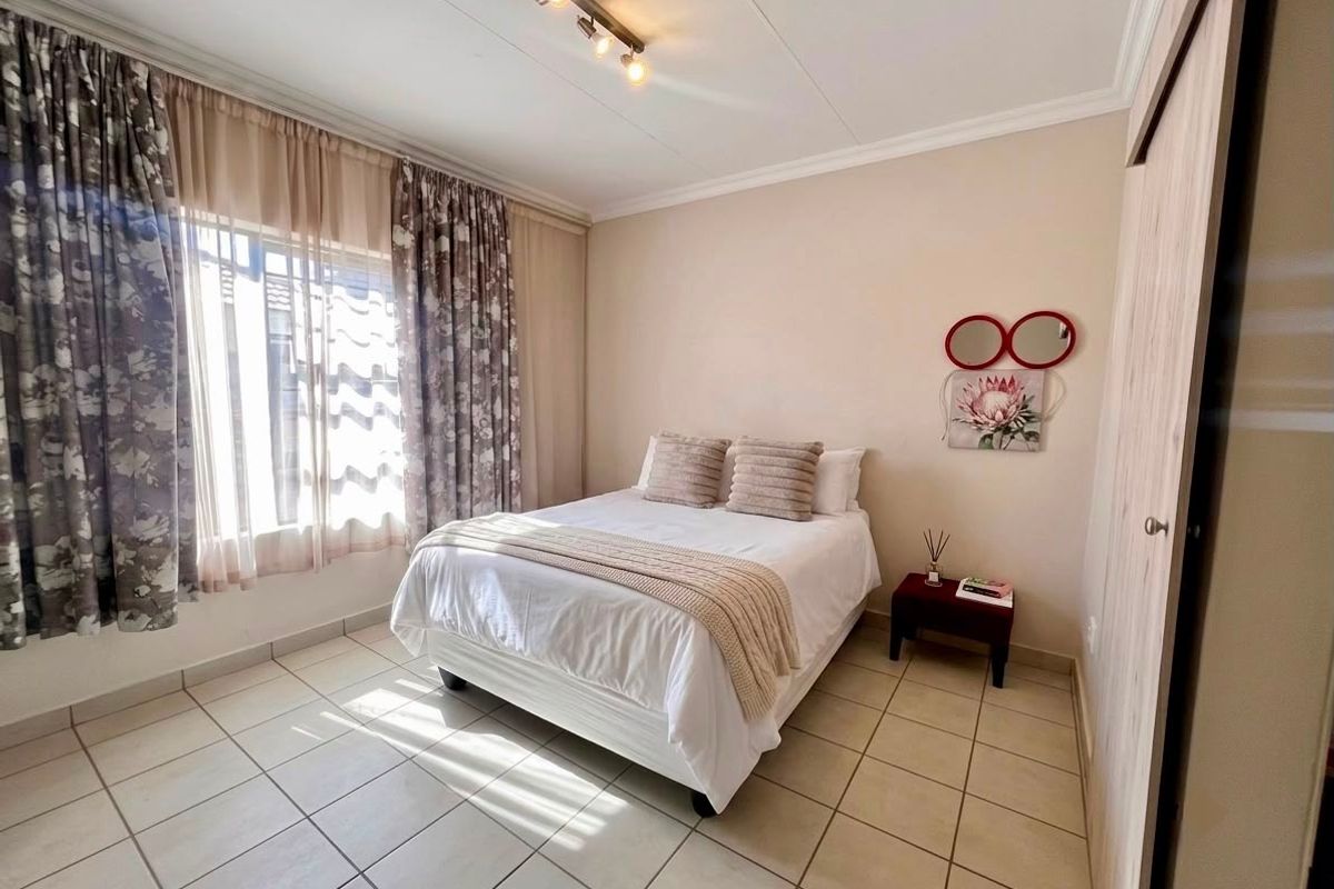 A well-maintained bedroom featuring neutral tiled flooring, built-in cupboards, and a ceiling-mounted spotlight fixture, offering a clean and functional living space.