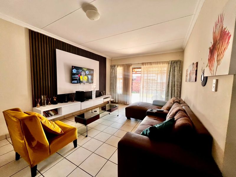 A well-maintained living room featuring a modern slatted wood accent wall, built-in media cabinetry, and ceramic tile flooring with direct access to the patio.