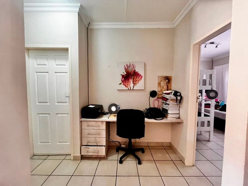 A functional home office area featuring a built-in desk with storage drawers and tiled flooring, situated in a neutral-toned space.