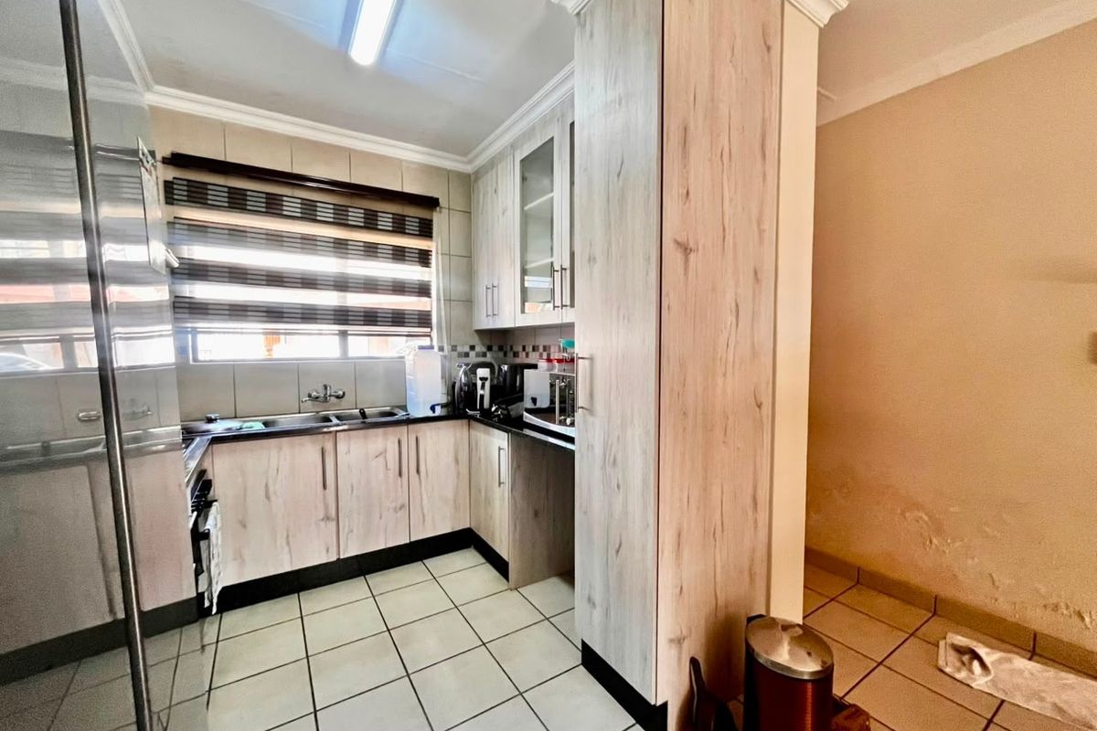 A functional kitchen featuring light wood-finish cabinetry, tiled flooring, and a double sink, with visible wall damage requiring attention.