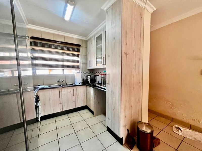 A functional kitchen featuring light wood-finish cabinetry, tiled flooring, and a double sink, with visible wall damage requiring attention.