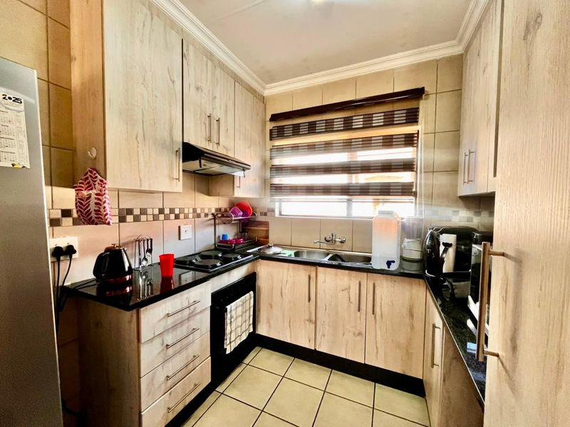 A functional kitchen featuring light wood-look cabinetry, dark granite countertops, a double basin sink, and a built-in hob with an extractor fan.