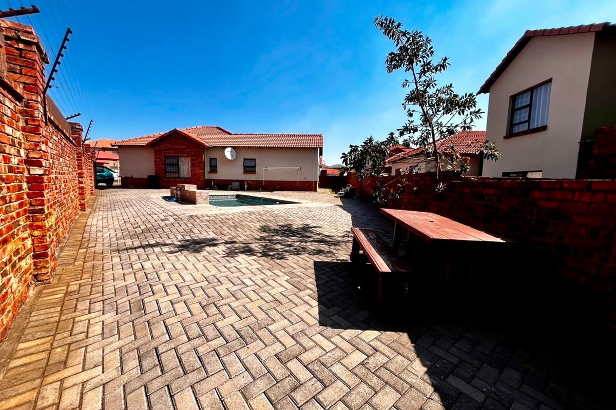 A spacious rear courtyard featuring a paved patio area, a private swimming pool, and secure brick boundary walls with electric fencing.